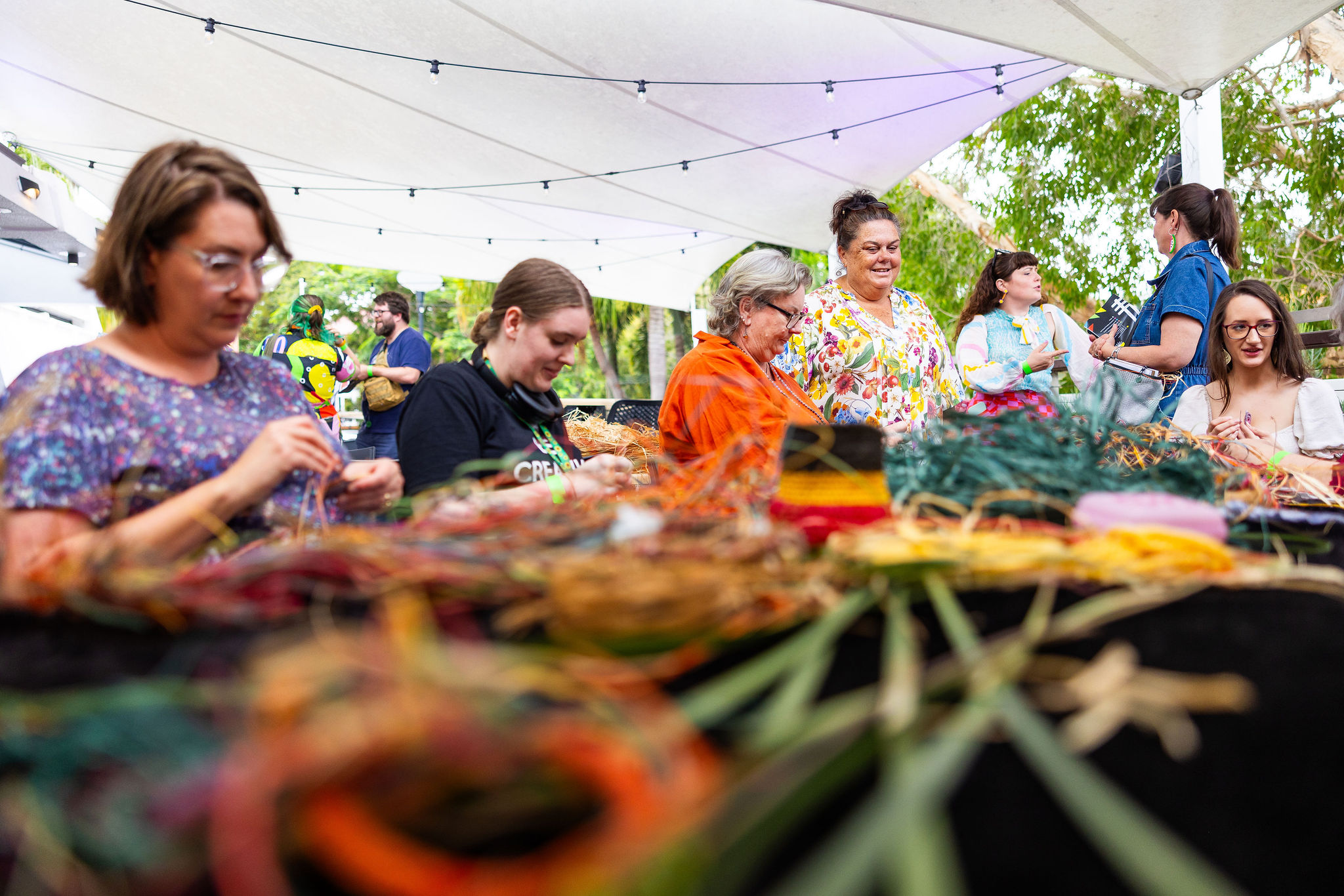 Community members weaving together at an outdoor workshop under a marquee